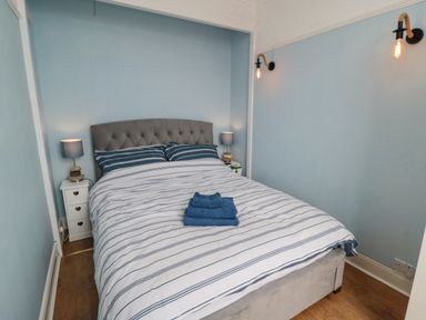 A bedroom with a double bed blue striped bedding lamps on bedside tables and wall lights at The Seahome in Scarborough