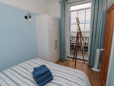 A bedroom with a striped bedspread folded towels on the bed a white wardrobe a telescope by the window and blue curtains at The Seahome in Scarborough