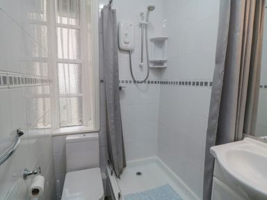 A bathroom with a toilet a shower with grey curtain a sink and a window at The Seahome in Scarborough