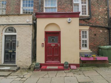 A red door with two potted plants on either side and a flower box with purple and yellow flowers on the right at The Seahome in Scarborough