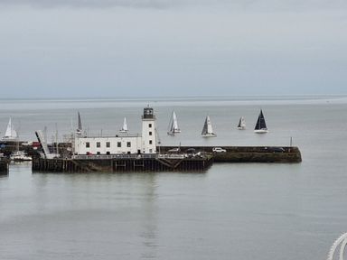 A lighthouse on a pier with cars and sailing boats in the water at The Seahome in Scarborough