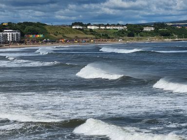 A view of waves in the sea with a beach and colorful beach huts on the shore at The Seahome in Scarborough