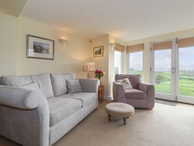 A living room with a grey sofa armchair round footstool side table lamp and flowers at Chase View Bowland Bridge near Bowness-On-Windermere