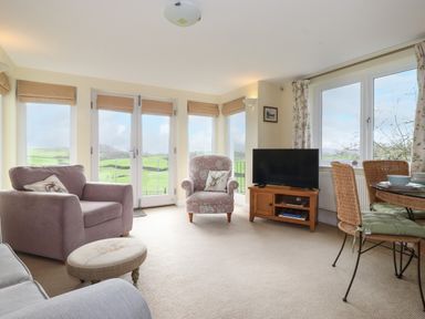 A living room with armchairs television and a dining table with chairs at Chase View Bowland Bridge near Bowness-On-Windermere
