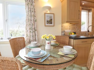 A dining area with a round glass table set with four place settings and yellow flowers in a jug at Chase View in Bowland Bridge near Bowness-On-Windermere