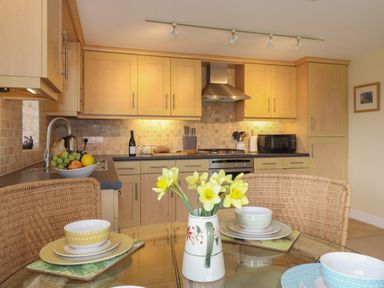 A kitchen with wooden cabinets a stove a microwave and a glass table with dishes and a vase of flowers at Chase View in Bowland Bridge near Bowness-On-Windermere