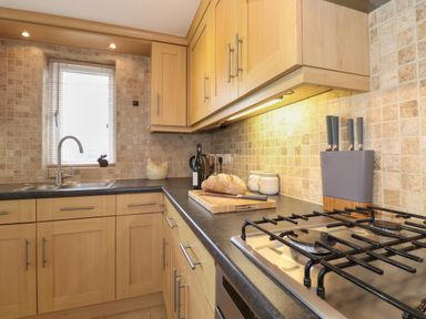 A kitchen with a gas stove a sink a loaf of bread on a cutting board and wooden cabinets at Chase View in Bowland Bridge near Bowness-On-Windermere