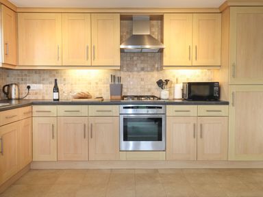 A kitchen with wooden cabinets a gas stove oven a microwave kettle bread and kitchen utensils on the counter at Chase View in Bowland Bridge near Bowness-On-Windermere