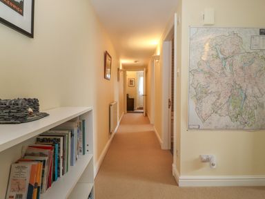 A hallway with bookshelves on the left wall a map on the right wall and framed pictures along the walls at Chase View Bowland Bridge near Bowness-On-Windermere