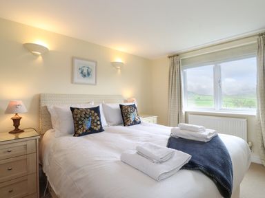 A bedroom with a made bed two peacock pillows bedside tables lamps and a window with a view at Chase View in Bowland Bridge near Bowness-On-Windermere