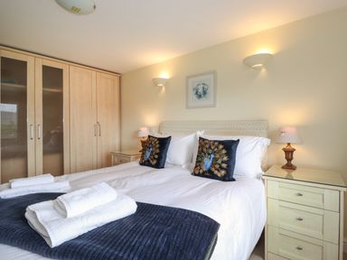 A bedroom with a bed featuring white linens and peacock pillows bedside tables with lamps and a large wardrobe at Chase View in Bowland Bridge near Bowness-On-Windermere