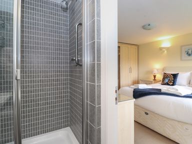 A shower area with grey tiled walls next to a bedroom with a bed and wooden wardrobe at Chase View Bowland Bridge near Bowness-On-Windermere