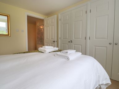 A bedroom with a bed and folded towels on white bedding near white closets at Chase View in Bowland Bridge near Bowness-On-Windermere