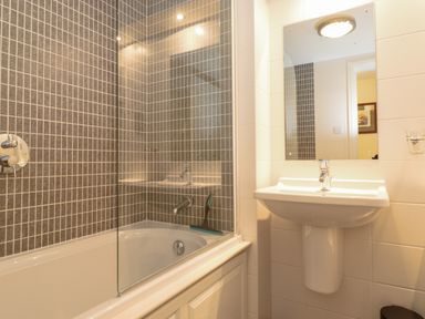 A bathroom with a bathtub shower combination and a sink with mirror at Chase View in Bowland Bridge near Bowness-On-Windermere