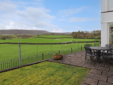 A patio with a round metal table and chairs overlooking green fields with stone walls at Chase View in Bowland Bridge near Bowness-On-Windermere