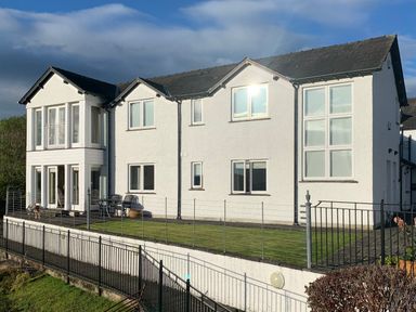 A white two-story house with multiple windows and a small fenced garden at Chase View in Bowland Bridge near Bowness-On-Windermere
