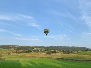 A hot air balloon flying over green fields and hills under a blue sky at Chase View in Bowland Bridge near Bowness-On-Windermere