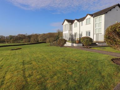 A white house with large windows and a lawn with bushes in front surrounded by trees at Chase View in Bowland Bridge near Bowness On Windermere