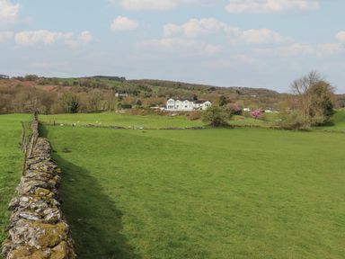 A field with a stone wall and sheep near a large white house with trees and hills in the background at Chase View in Bowland Bridge near Bowness-On-Windermere