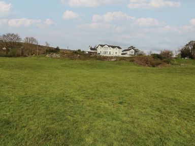 A field with green grass and a white house on a hill in the background at Chase View Bowland Bridge near Bowness-On-Windermere