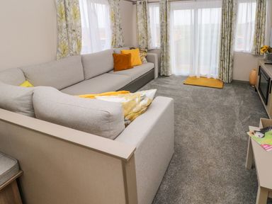 A living room with a large grey sectional sofa yellow cushions curtains and a carpet at The Waves in Little Haven near Broad Haven