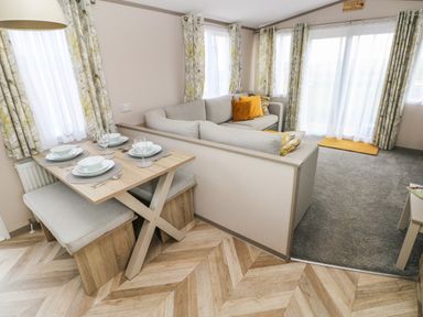 A dining area with table set for four beside a corner sofa with cushions in a living room at The Waves in Little Haven near Broad Haven