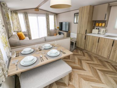 A dining area with a set table next to a living room with a sofa and a television and a kitchen with wooden cabinets at The Waves in Little Haven near Broad Haven