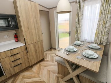 A kitchen and dining area with wooden cabinets a table set for four and a door with curtains at The Waves in Little Haven near Broad Haven