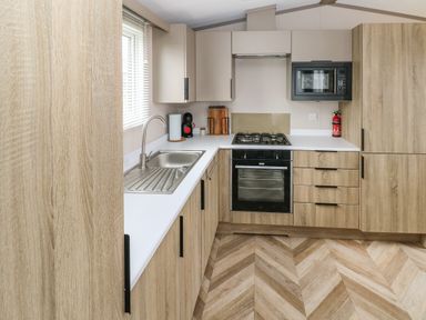A kitchen with wooden cabinets a gas stove an oven a microwave a sink and a coffee machine at The Waves in Little Haven near Broad Haven