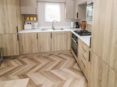 A kitchen with wooden cabinets a white countertop a sink a gas stove an oven a toaster a kettle and a coffee machine at The Waves in Little Haven near Broad Haven