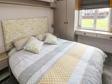 A bedroom with a patterned bedspread and pillows next to a window and wardrobe at The Waves in Little Haven near Broad Haven
