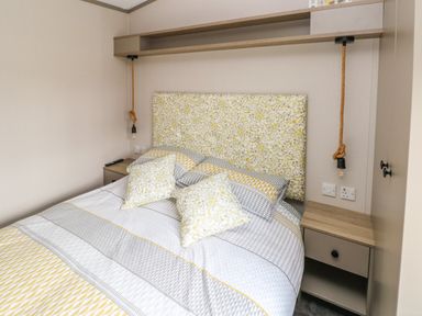 A bedroom with a bed with patterned headboard and pillows and two bedside tables with hanging lights at The Waves in Little Haven near Broad Haven