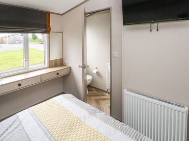 A bedroom with a bed a window with blinds a wall-mounted television and an open door to a bathroom at The Waves in Little Haven near Broad Haven