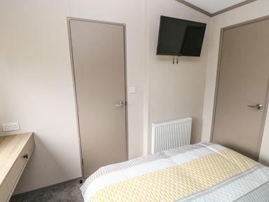 A bedroom with two closed doors a wall-mounted TV a radiator a desk and a bed with patterned bedding at The Waves in Little Haven near Broad Haven