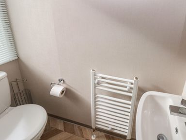 A bathroom with a toilet paper holder a towel radiator sink and a window with blinds at The Waves in Little Haven near Broad Haven