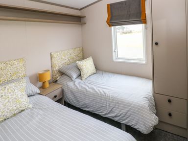 A bedroom with two single beds a nightstand with a lamp a window with a blind and a wardrobe at The Waves in Little Haven near Broad Haven