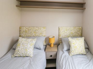 A bedroom with two single beds with patterned headboards and pillows separated by a nightstand with a yellow lamp at The Waves in Little Haven near Broad Haven