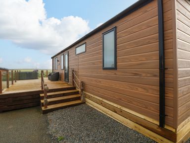 An exterior view of a wooden clad building with steps leading to a deck with chairs and a hot tub at The Waves in Little Haven near Broad Haven