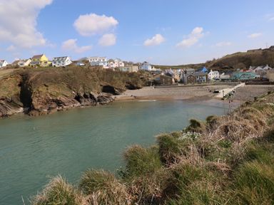 A coastal village with houses on a hill and a beach with water at The Waves in Little Haven near Broad Haven