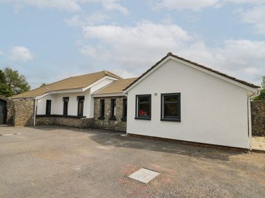A single story house with white and stone walls and a tiled roof on a paved area at Heritage in St Clears