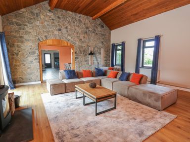 A living room with a large sectional sofa with blue and orange cushions a wooden coffee table and a stone wall at Heritage in St Clears