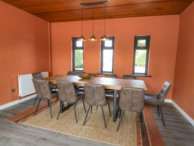 A dining room with a rectangular wooden table and eight brown chairs on a rug with three pendant lights hanging above the table at Heritage St Clears