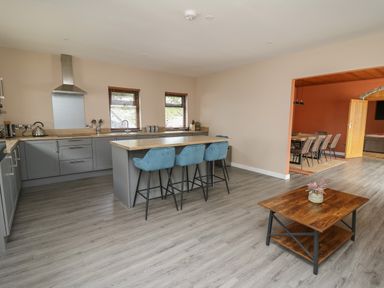 A kitchen with an island with three blue bar stools and a wooden coffee table in the foreground at Heritage in St Clears