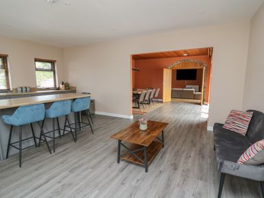 An open living space with a kitchen counter with blue bar stools a wooden coffee table a grey sofa with striped cushions and a dining area with chairs and a television in the background at Heritage in St Clears