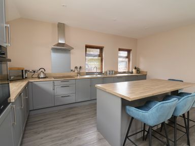 A kitchen with grey cabinets wooden countertops two windows and a kitchen island with blue chairs at Heritage in St Clears
