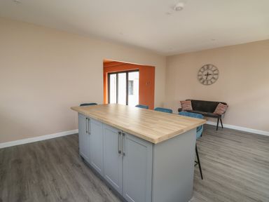 A dining area with a kitchen island surrounded by blue chairs and a black bench under a clock at Heritage in St Clears