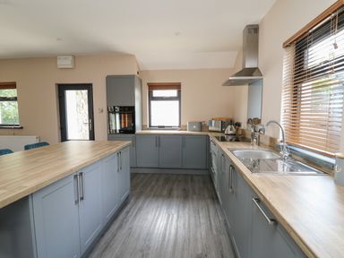 A kitchen with gray cabinets wooden countertops a sink stove and windows with blinds at Heritage in St Clears