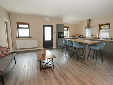 An open kitchen and living area with a wooden coffee table four blue bar stools an oven and a door with windows at Heritage in St Clears