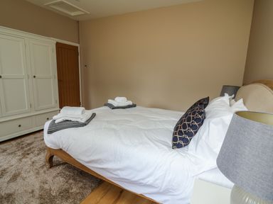 A bedroom with a bed with white bedding and folded towels a white wardrobe and a lamp on a bedside table at Heritage in St Clears