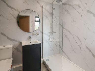 A bathroom with a toilet a black vanity with sink a round mirror and a shower at Heritage in St Clears